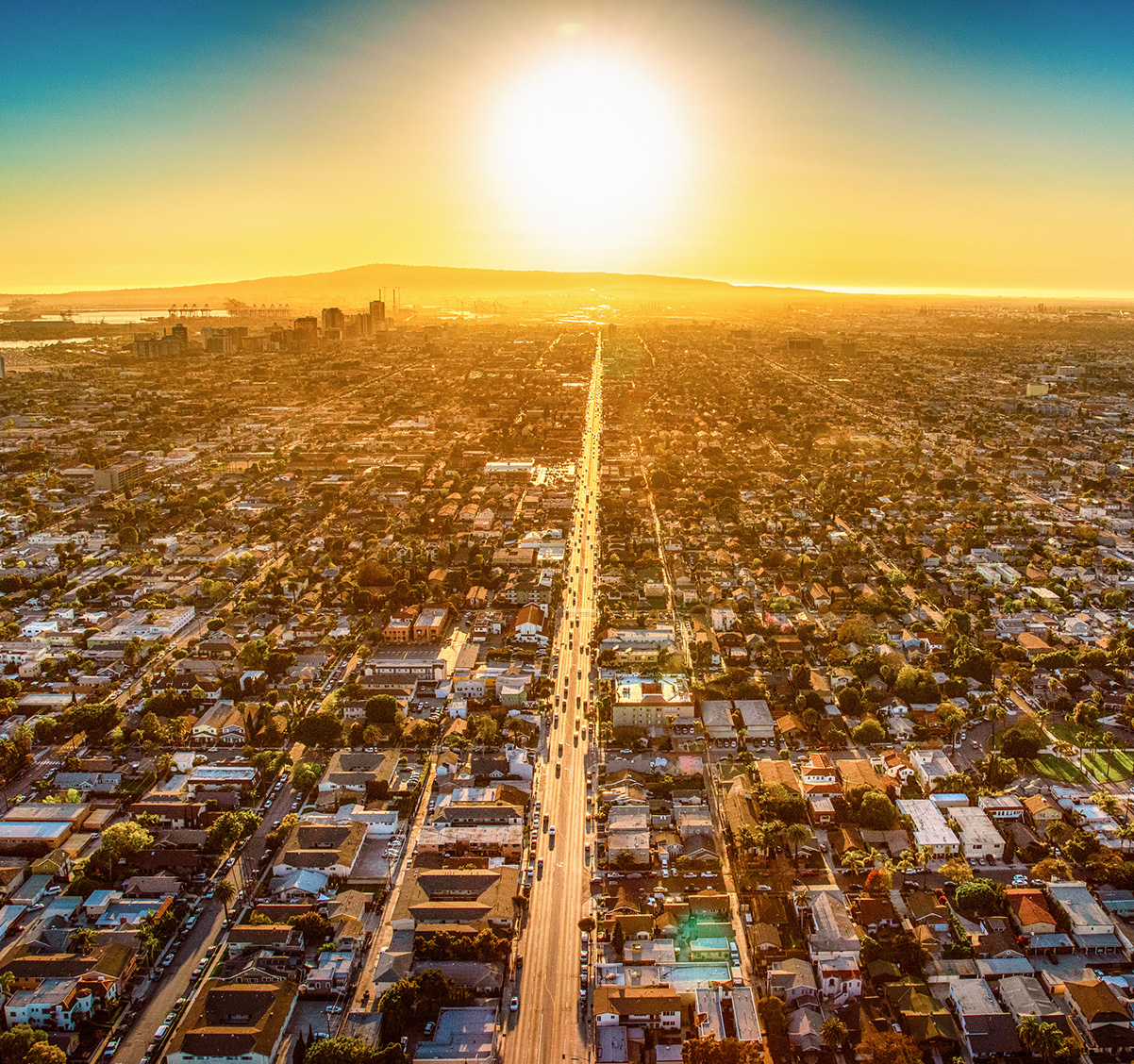 Aerial view of Los Angeles with a bright orange sunset in the distance.